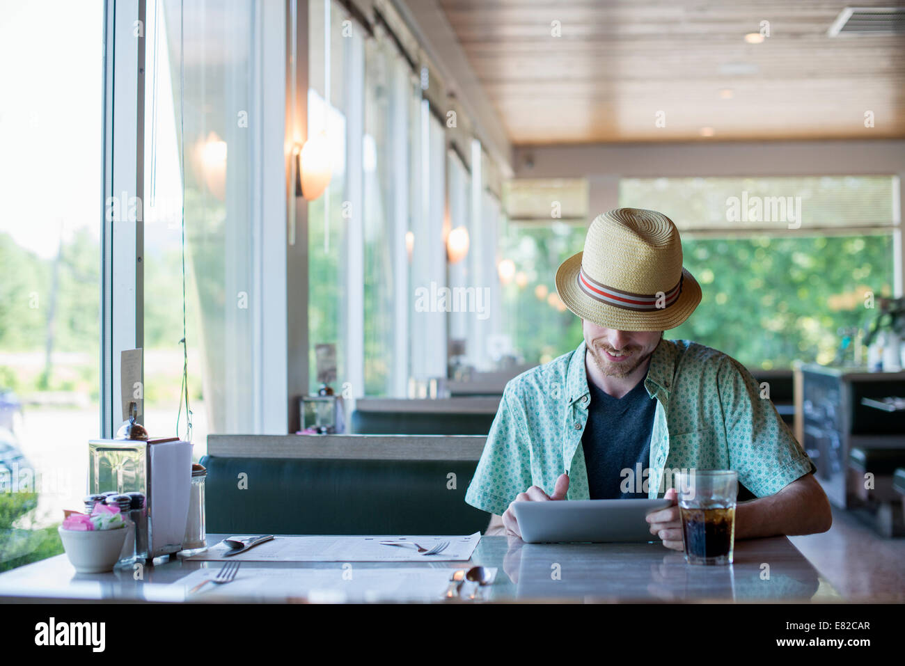 Ein Mann trägt einen Hut sitzt in einem Diner mit einem digitalen Tablet. Stockfoto