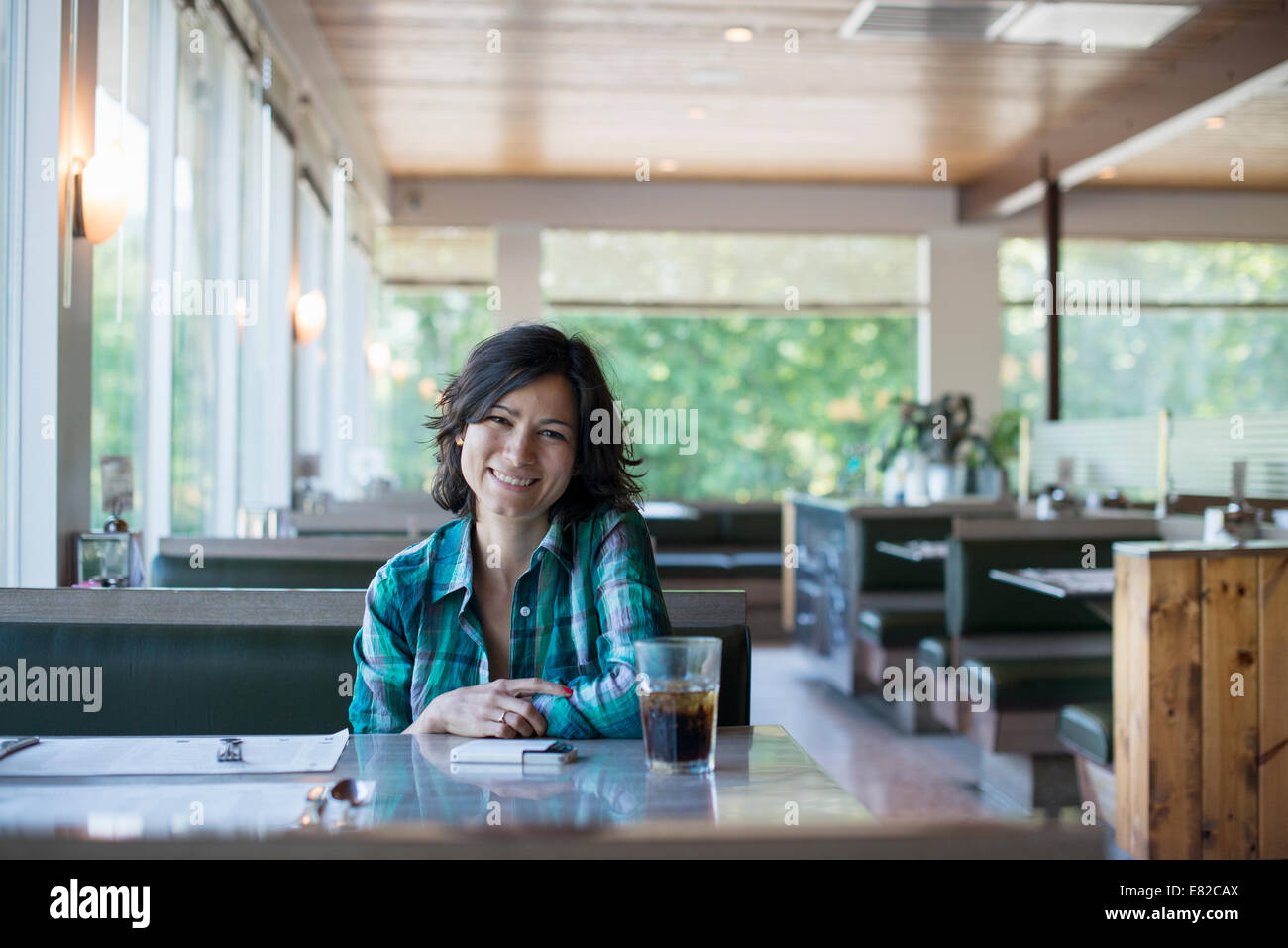 Eine Frau in ein kariertes Hemd an einem Tisch sitzen, lachen und mit Blick auf ihr Smartphone. Stockfoto