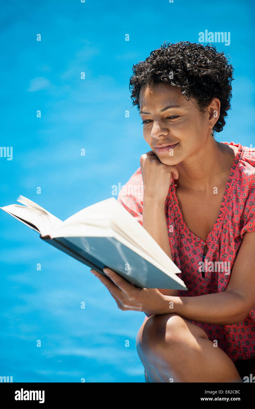 Eine Frau sitzt in einem Schwimmbad, ein Buch zu lesen. Stockfoto