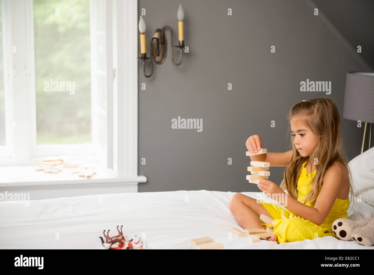 Ein Mädchen sitzt auf einem Bett mit Bausteinen zu spielen. Stockfoto