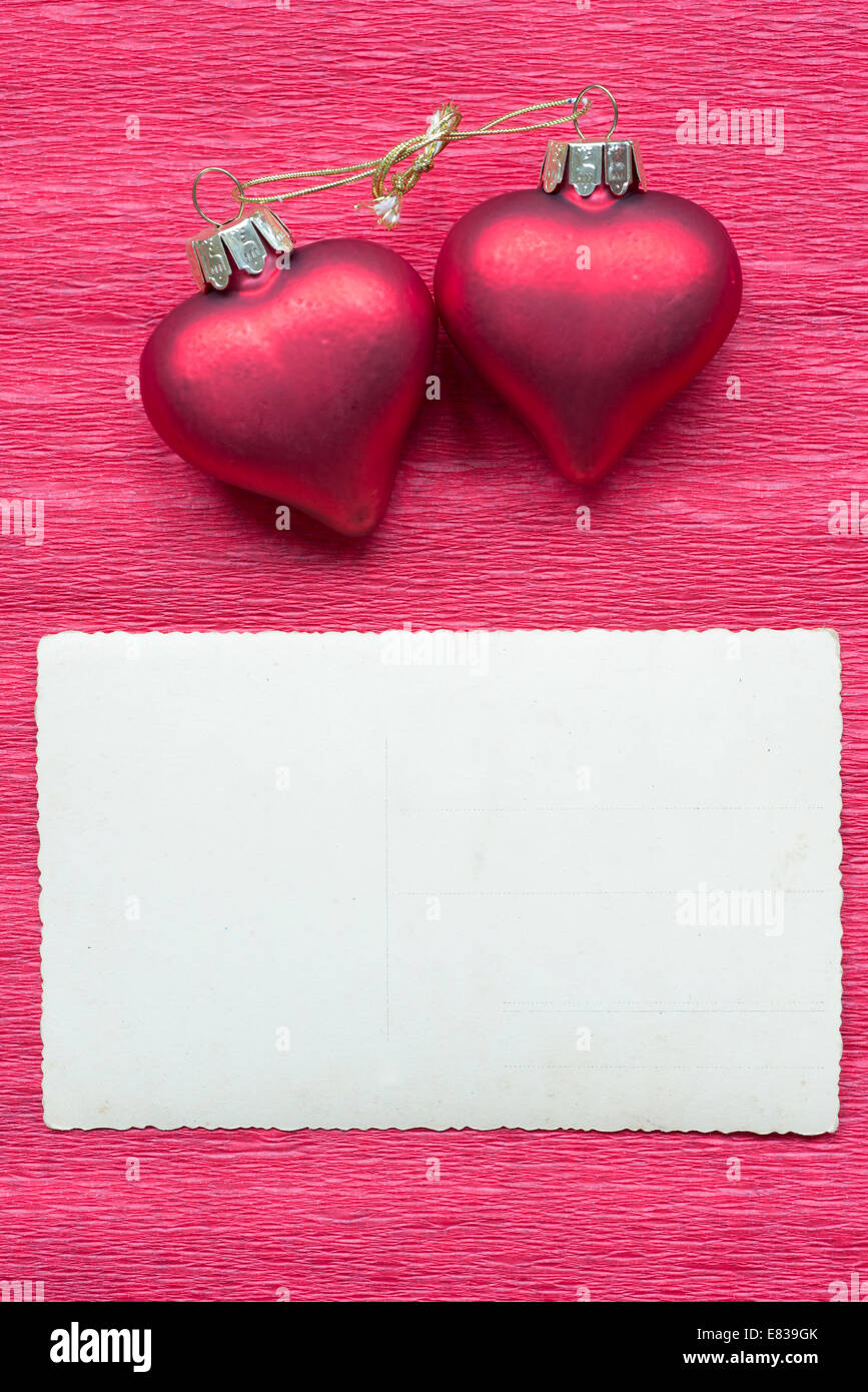 zwei verknüpfte Herzen mit Postkarte auf rotem Papierhintergrund Stockfoto