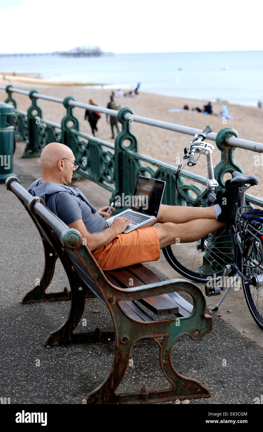 Hove Brighton UK - Mann sitzt am Meer Bank in Hove arbeiten auf einem Laptop-Computer Stockfoto