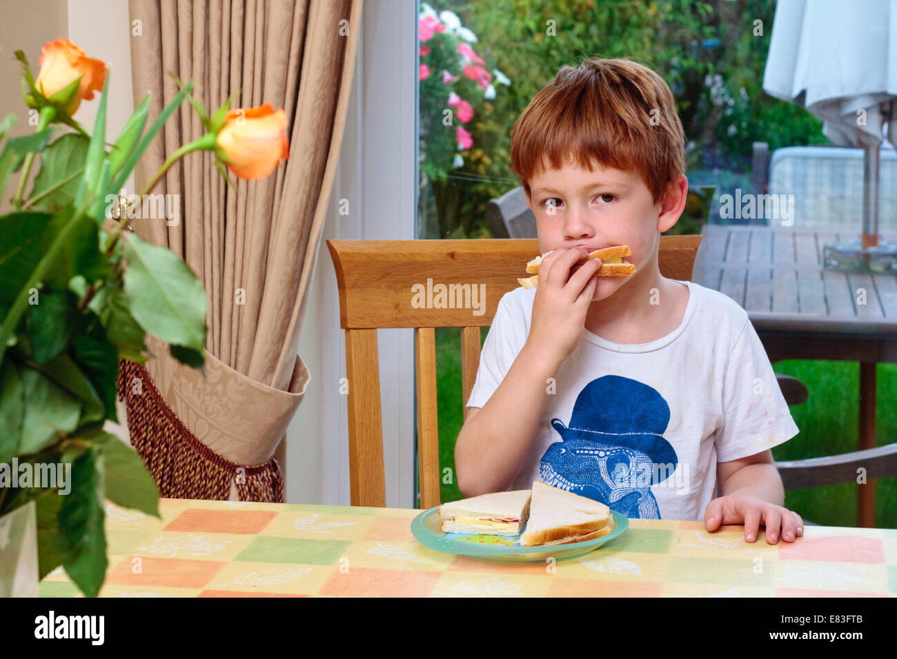 Ein kleiner Junge saß an einem Tisch essen einen sandwich Stockfoto