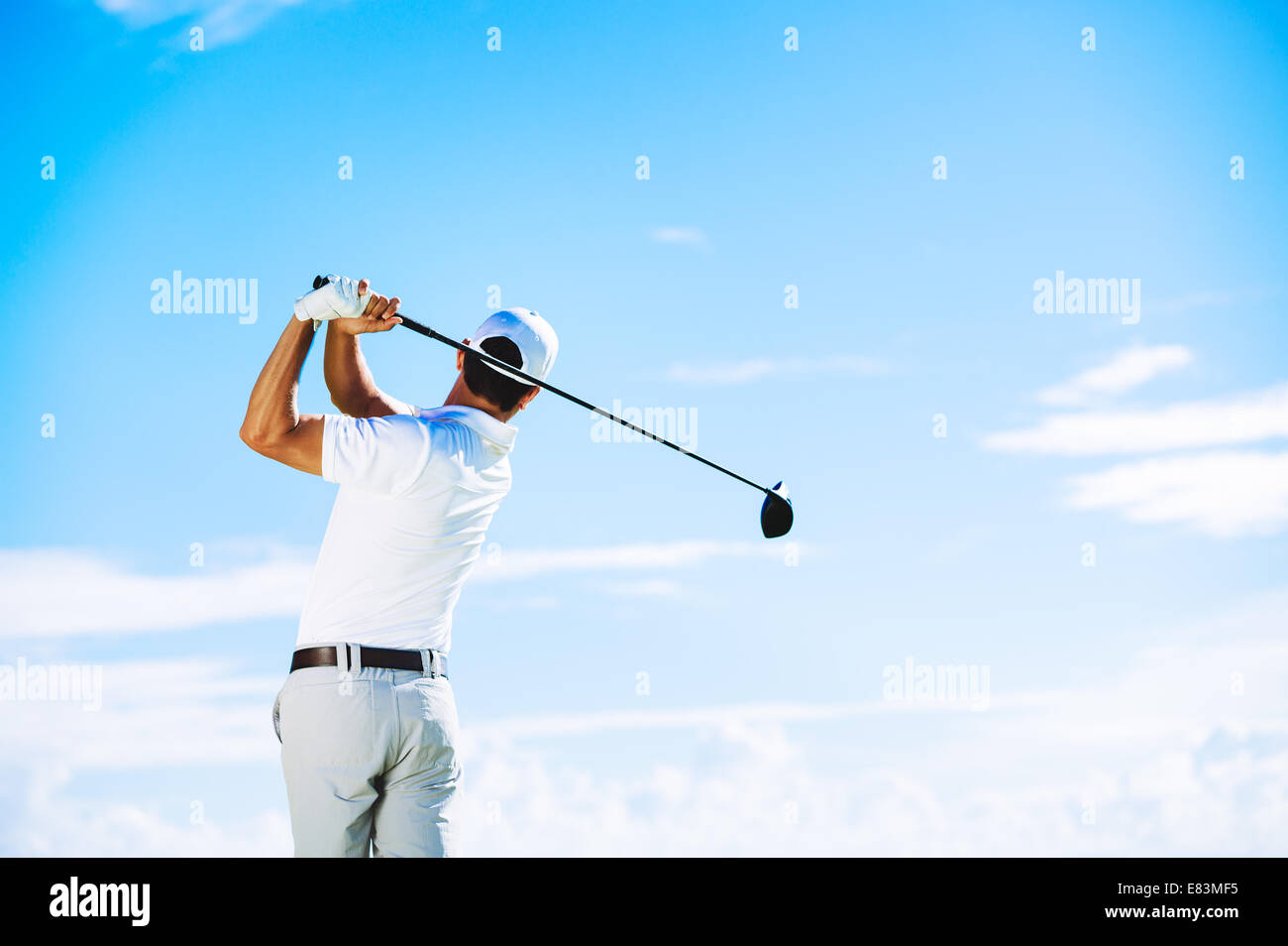 Man schwingt Golfclub mit blauem Himmelshintergrund Stockfoto