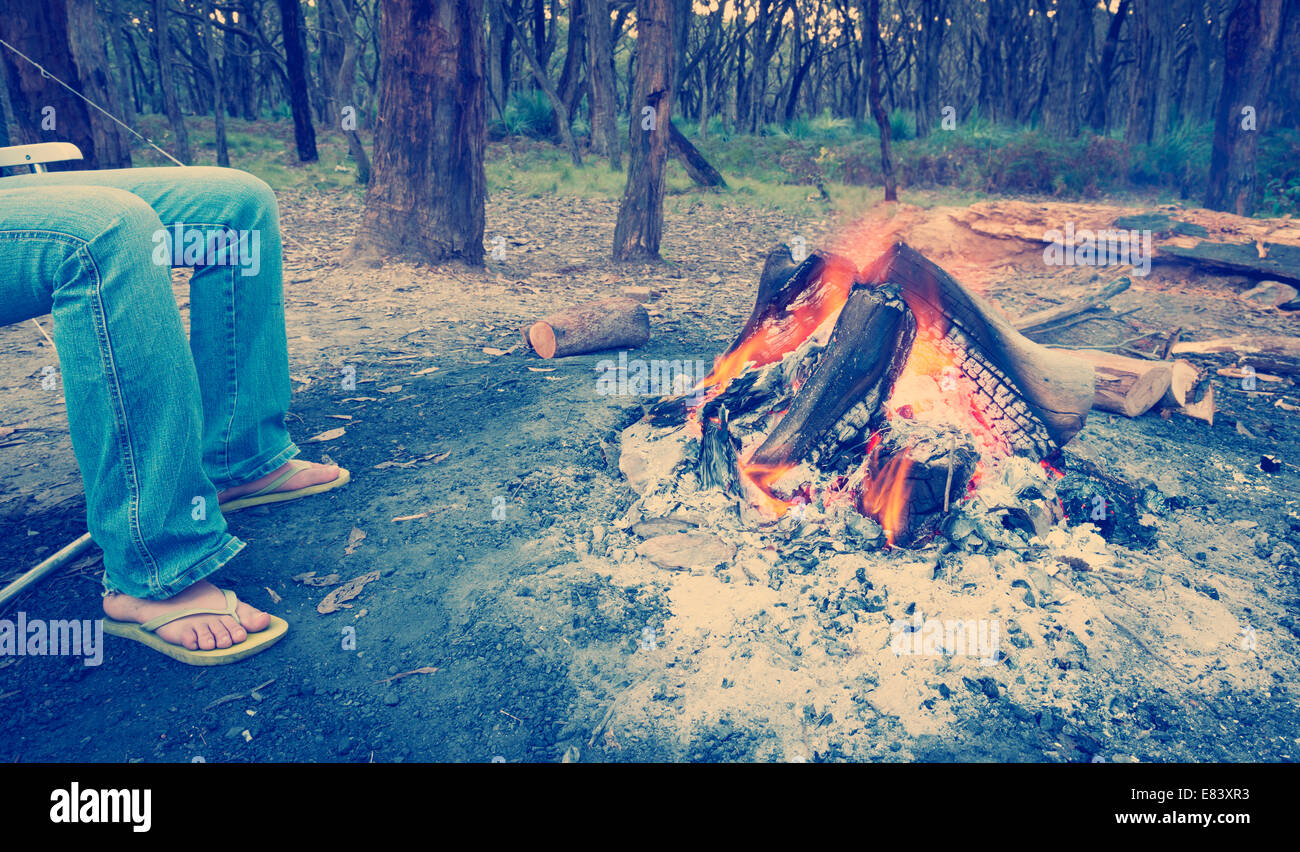 Person wärmt ihre Füße neben einem Lagerfeuer bei Abenddämmerung camping im Wald mit Instagram-Stil-filter Stockfoto