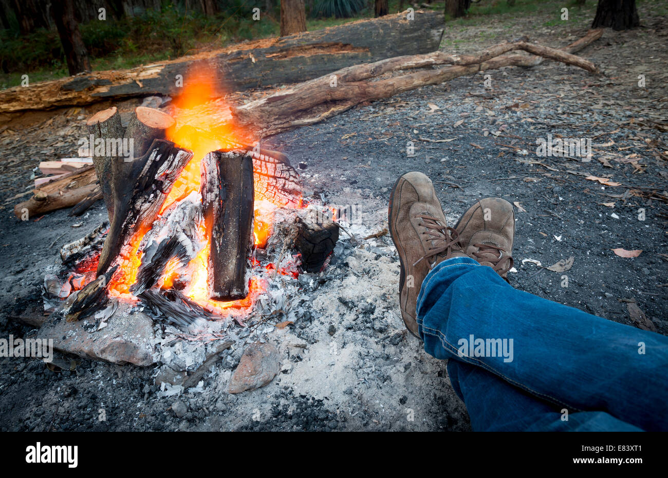 Person wärmt ihre Füße neben einem Lagerfeuer bei Abenddämmerung camping im Wald Stockfoto