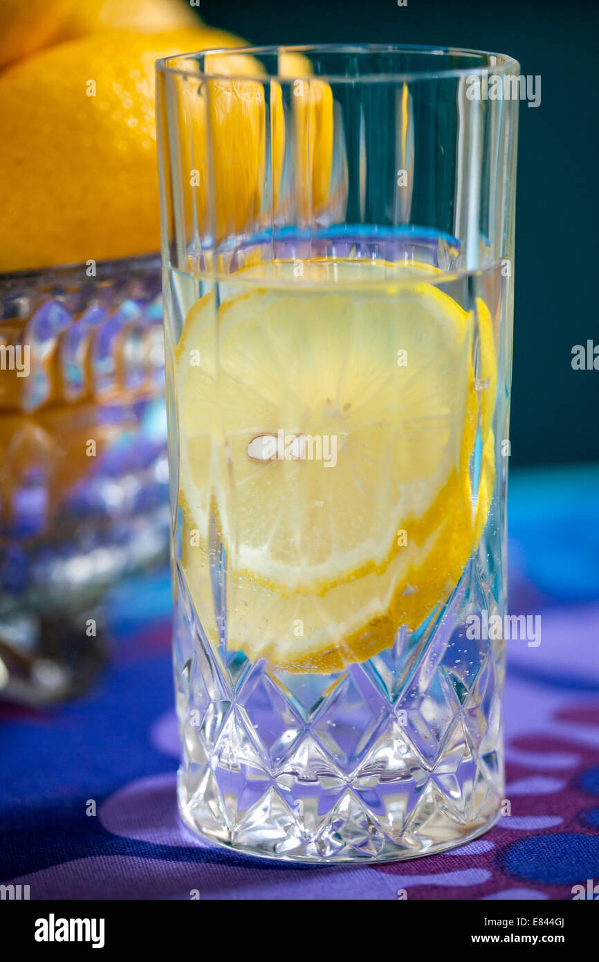 Zitronenwasser in Glas, Zitronenscheiben in Glas Wasser, Schale der Zitronen im Hintergrund Stockfoto