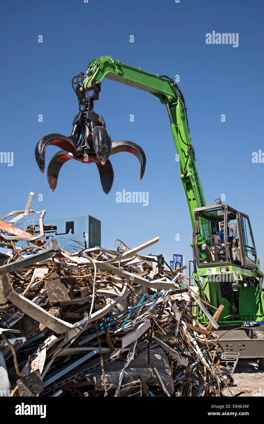 Schwere Maschine greift nach einem Berg von Schrott auf dem Gelände einer Recyclinganlage. Stockfoto