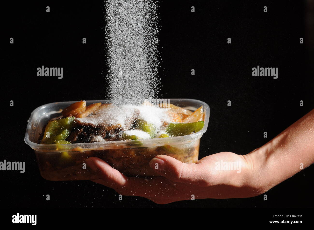 Speisen zum Mitnehmen mit Salz auf von oben gegossen wird. Hohe Niveaus des Salzes in Junk-Food verursachen, Bluthochdruck und Herz-Kreislauferkrankungen Stockfoto
