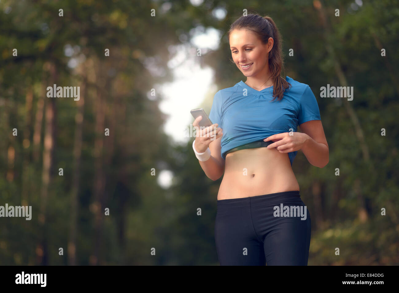 Junge sportliche Frau trainieren im Wald stehen, die ihr Smartphone zu betrachten, wie sie eine mobile Anwendung elektronischer nutzt Stockfoto