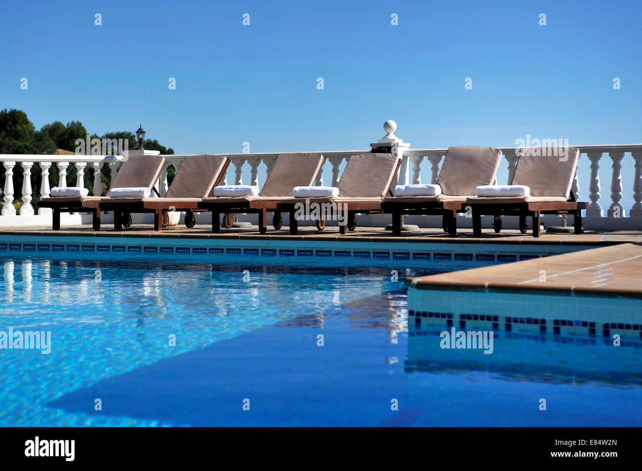 sechs Liegestühle an der Seite eines Schwimmbades in der Sonne und blauer Himmel Stockfoto