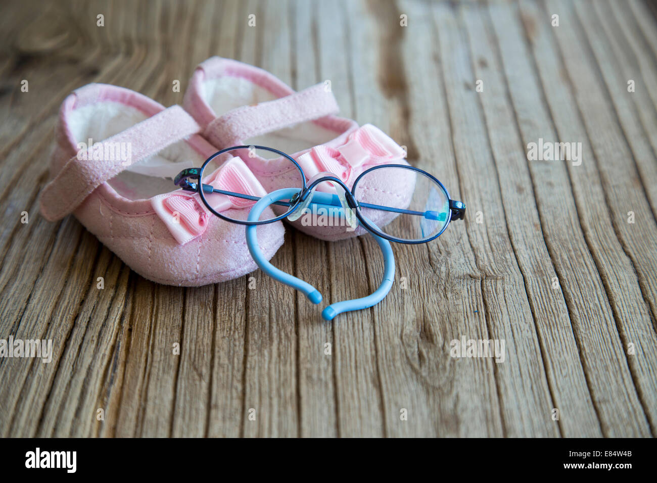 Süßer rosa Baby-Schuhe und Brillen auf den hölzernen Hintergrund Stockfoto