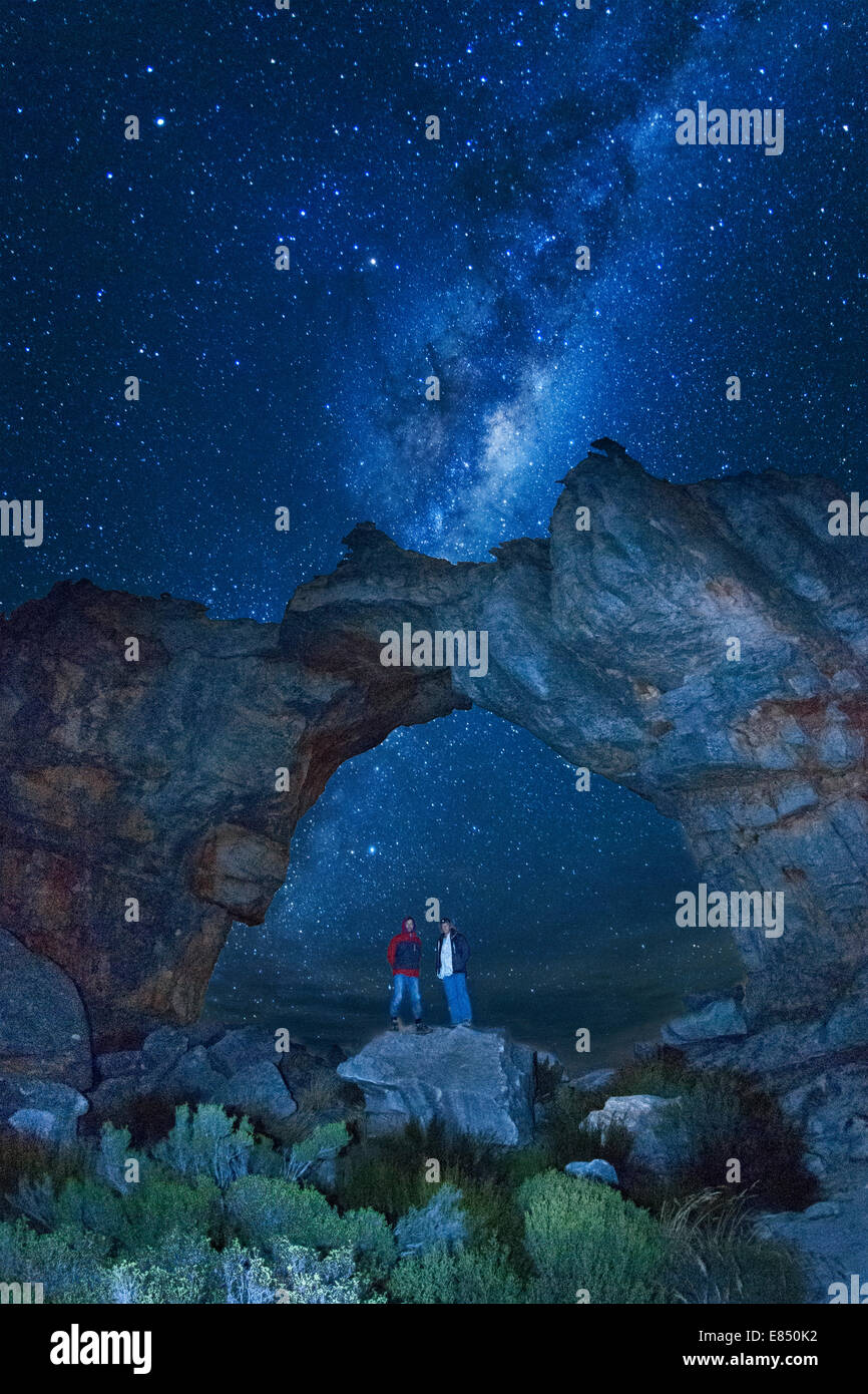 Die Milchstraße und zwei Männer stehen unter dem Wolfsberg-Bogen in den Cederbergen in Südafrika. Stockfoto