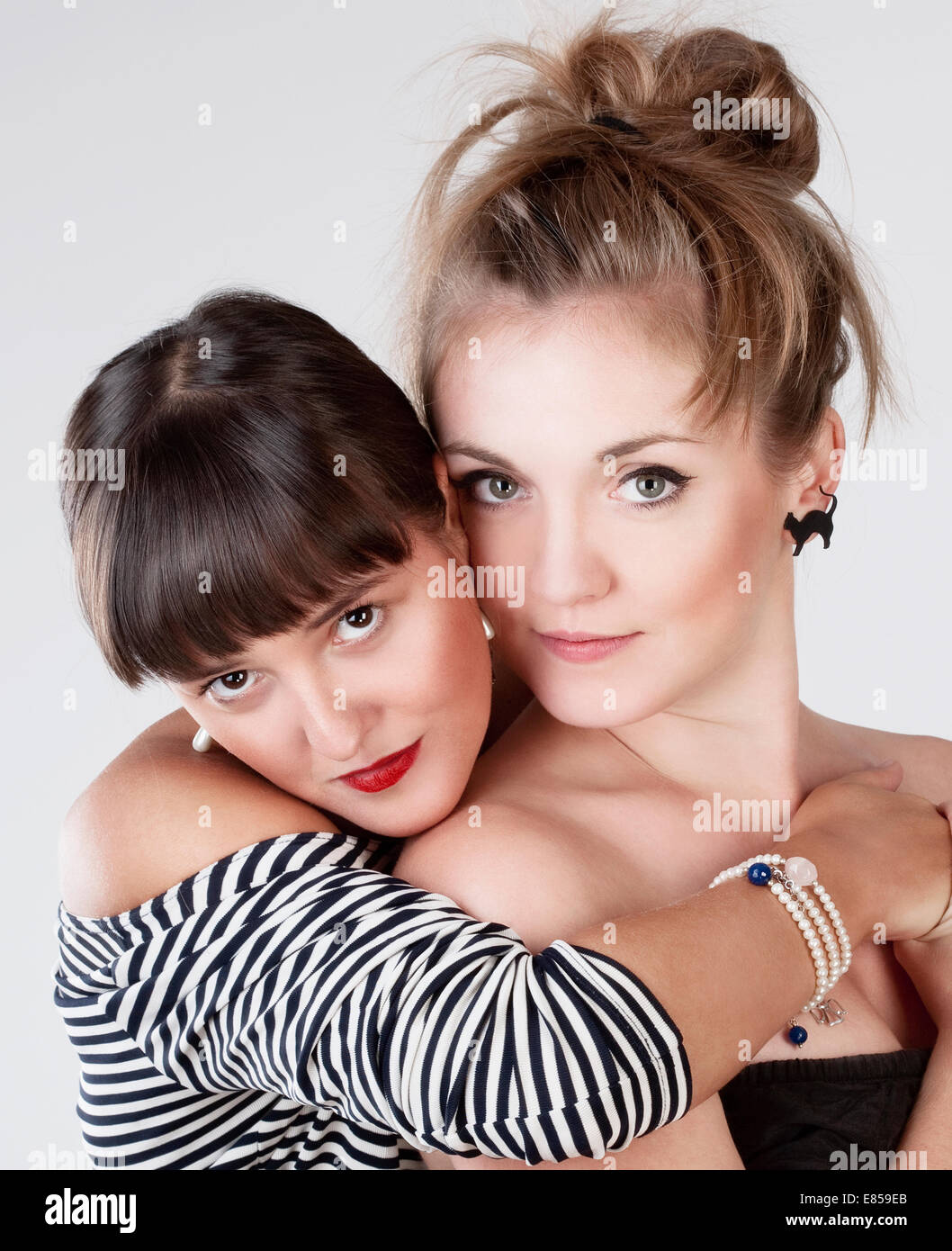 Zwei junge Freundinnen umarmen - isoliert auf grau Stockfoto