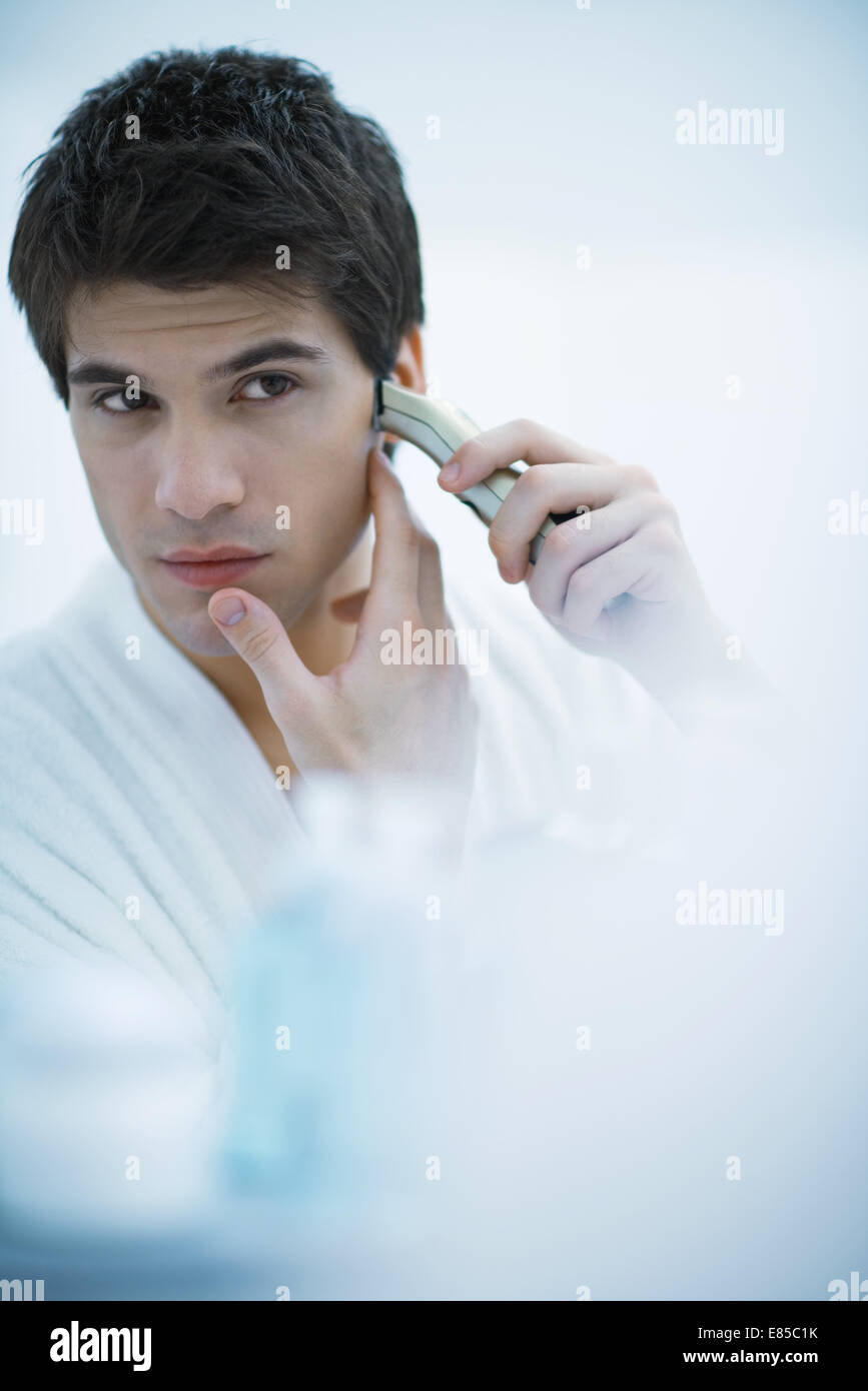 Junger Mann in Spiegel, mit elektrischen Rasierapparat Rasieren Stockfoto