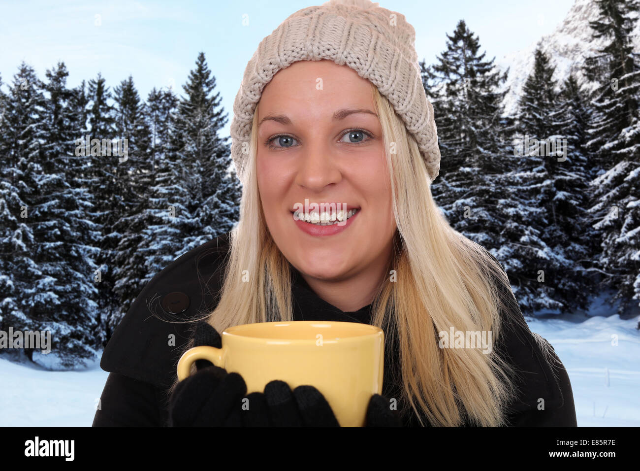 Lächelnde blonde Frau Trinkbecher Tee outdoor im Wald im winter Stockfoto