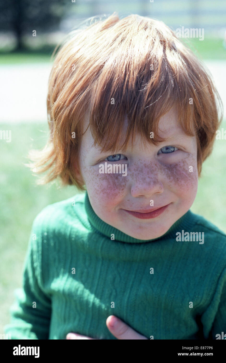Ein vier-jährige amerikanische junge mit roten Haaren, blauen Augen und ein sommersprossiges Gesicht lächelt in die Kamera für dieses informelle outdoor Portrait. Stockfoto