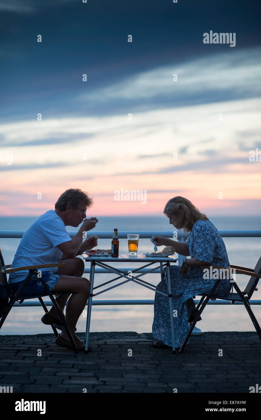 Ein paar saß Essen ihr Abendessen unter freiem Himmel auf der Promenade in Aberystwyth nach Sonnenuntergang auf einem warmen Juli Sommerabend Wales UK Stockfoto