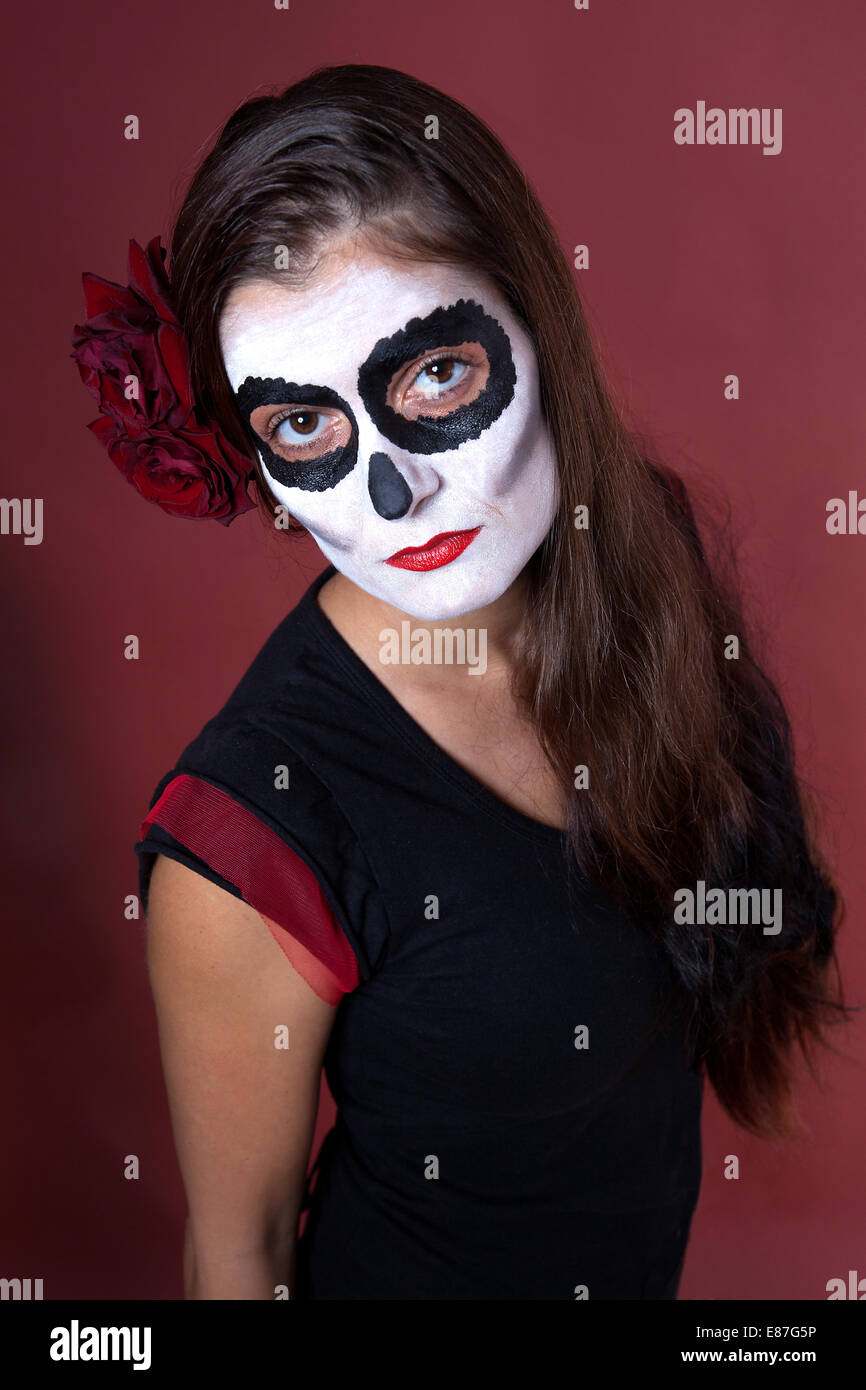 Frau mit Make-up von la Santa Muerte mit roten Rosen vor einem roten Hintergrund Stockfoto