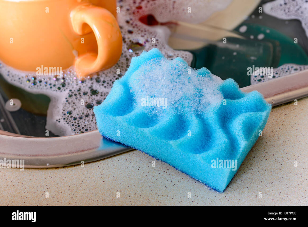 Reinigung das schmutzige Geschirr mit einem blauen Schwamm mit Waschmittel im Waschbecken Stockfoto