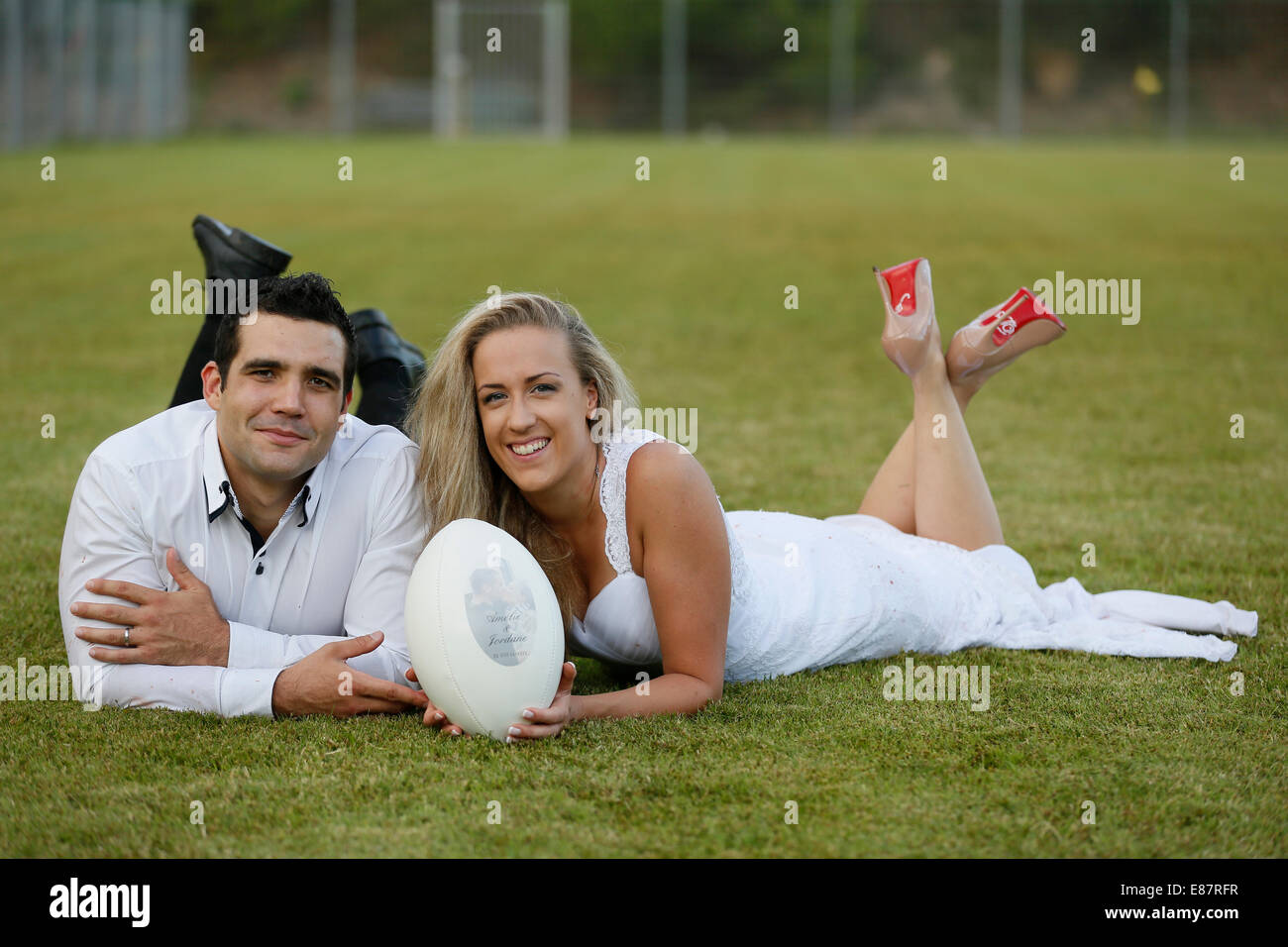 Trash, Kleid, Braut und Bräutigam liegend auf einem Rugby-Spielfeld mit einem Rugby-ball Stockfoto