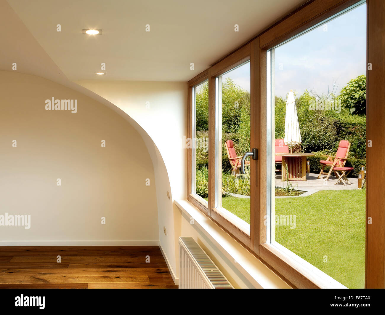 modernes Interieur mit Holzboden und einem Esstisch mit Stühlen, Sonnenschirm in einem üppigen Garten außerhalb Stockfoto