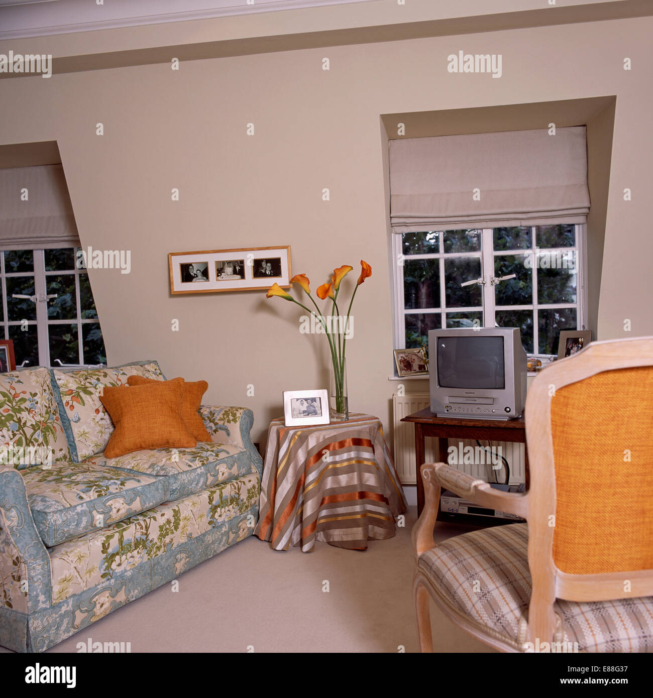 Fernsehen am Tisch vor Fenster mit blinden in kleinen Dachboden Wohnzimmer mit gemustertem blauen Sofa beige Stockfoto