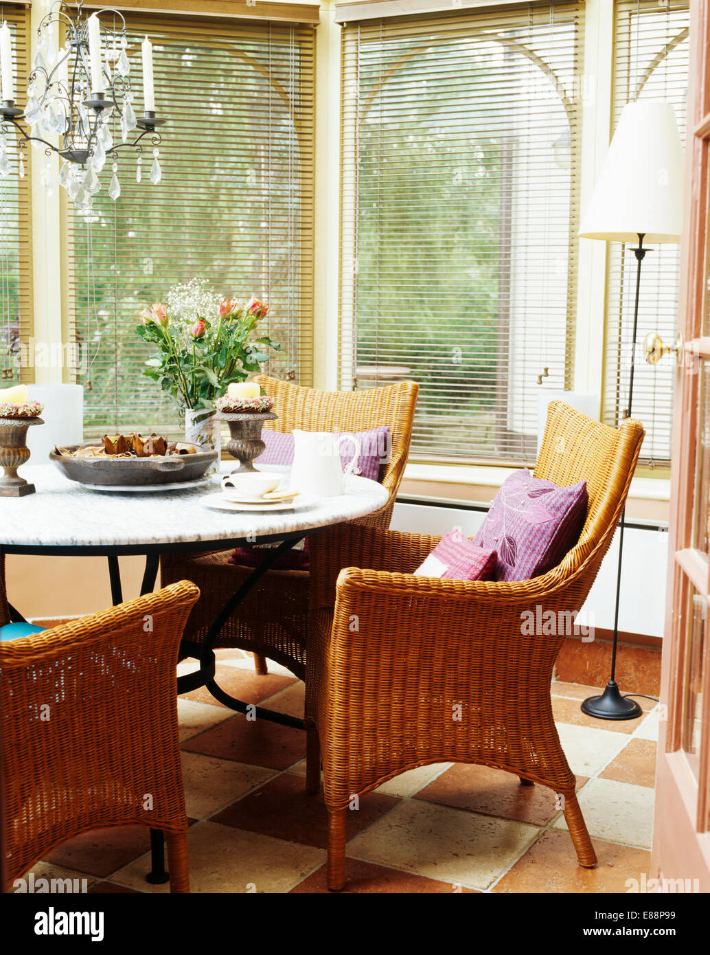 Wicker Sessel am runden Tisch im Wintergarten mit Jalousien an den Fenstern Stockfoto