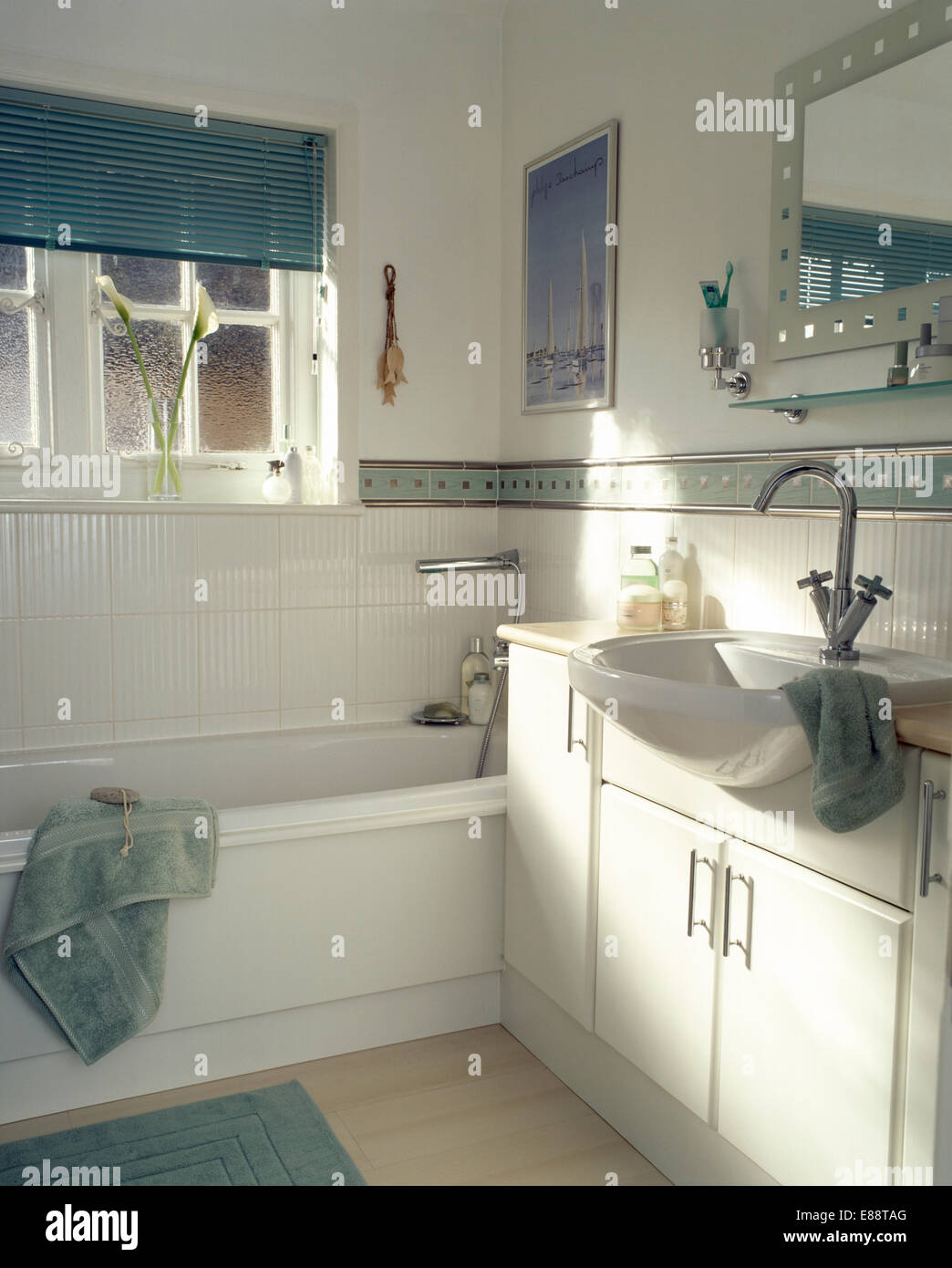 Blasses Grün Jalousie am Fenster über der Badewanne im modernen Badezimmer mit grünen und silbernen Rand-Fliesen Stockfoto
