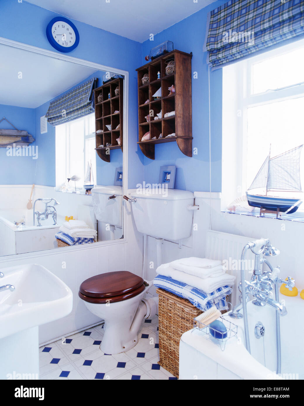 Großer Spiegel an der Wand neben der Toilette in kleinen blauen Badezimmer mit gefaltete Handtücher auf Wäsche Weidenkorb unter Fenster Stockfoto