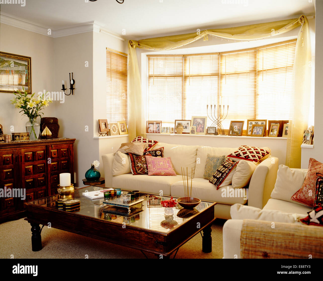 Sahne Sofa mit gemusterten Kissen unter Fenster im Wohnzimmer mit Glasplatte Holz Couchtisch Stockfoto