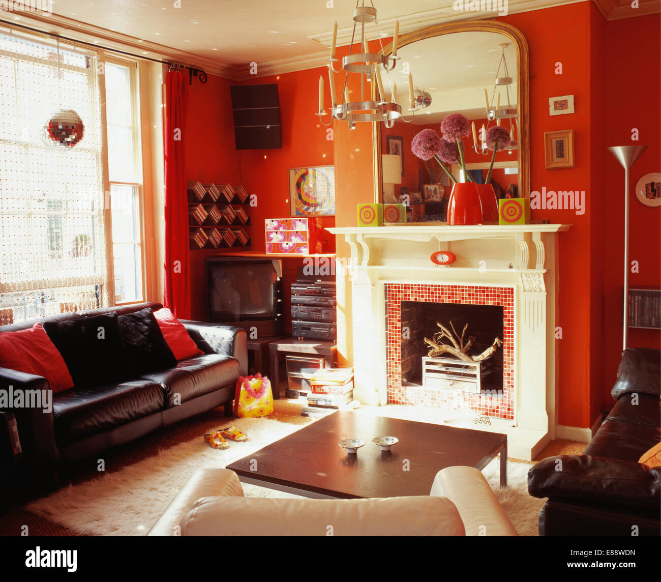 Braune Ledercouch unter Fenster in rote Salon mit großem Spiegel über weißen Kamin Stockfoto