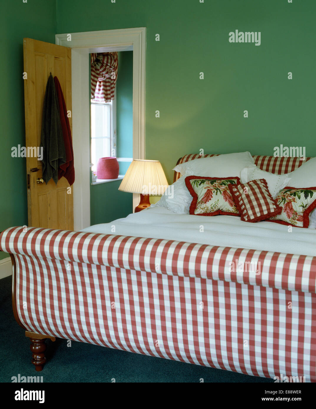 Rot + weiß überprüft Polsterbett mit floralen und aufgegebenen Kissen in grün Schlafzimmer Stockfoto