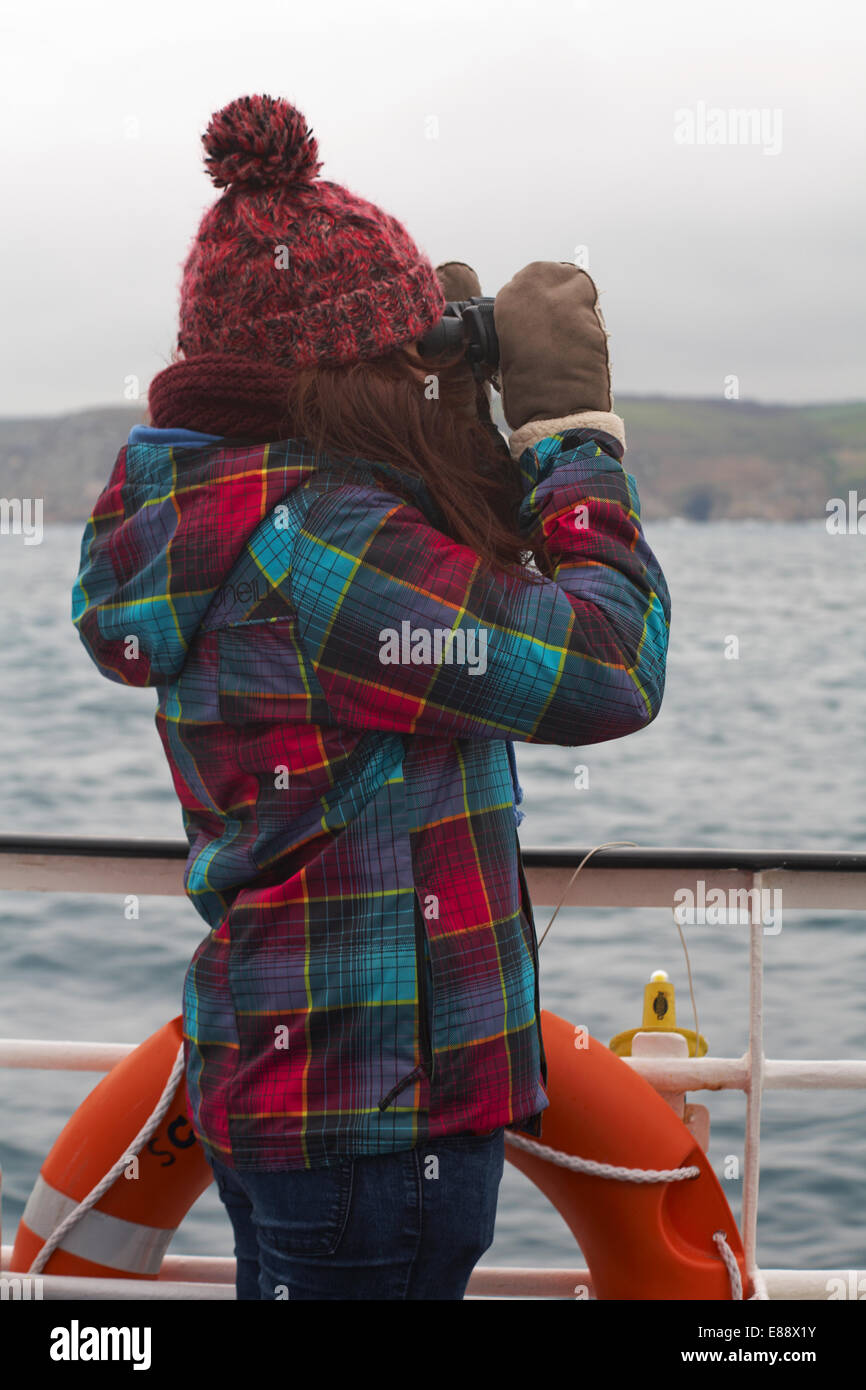 Junge Frau, die durch ein Fernglas an Bord des RMV Scillonian III Überschrift für die Scilly-inseln, Scillies, Cornwall im April Stockfoto
