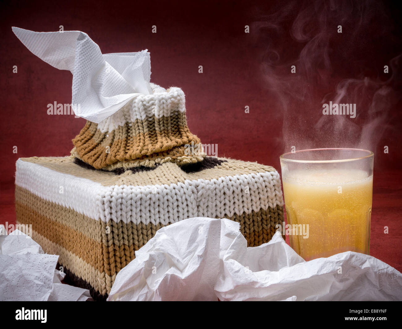 Tissue box in Strick Ummantelung und heiße Grippe Medizin trinken über dunkelroten Hintergrund Stockfoto