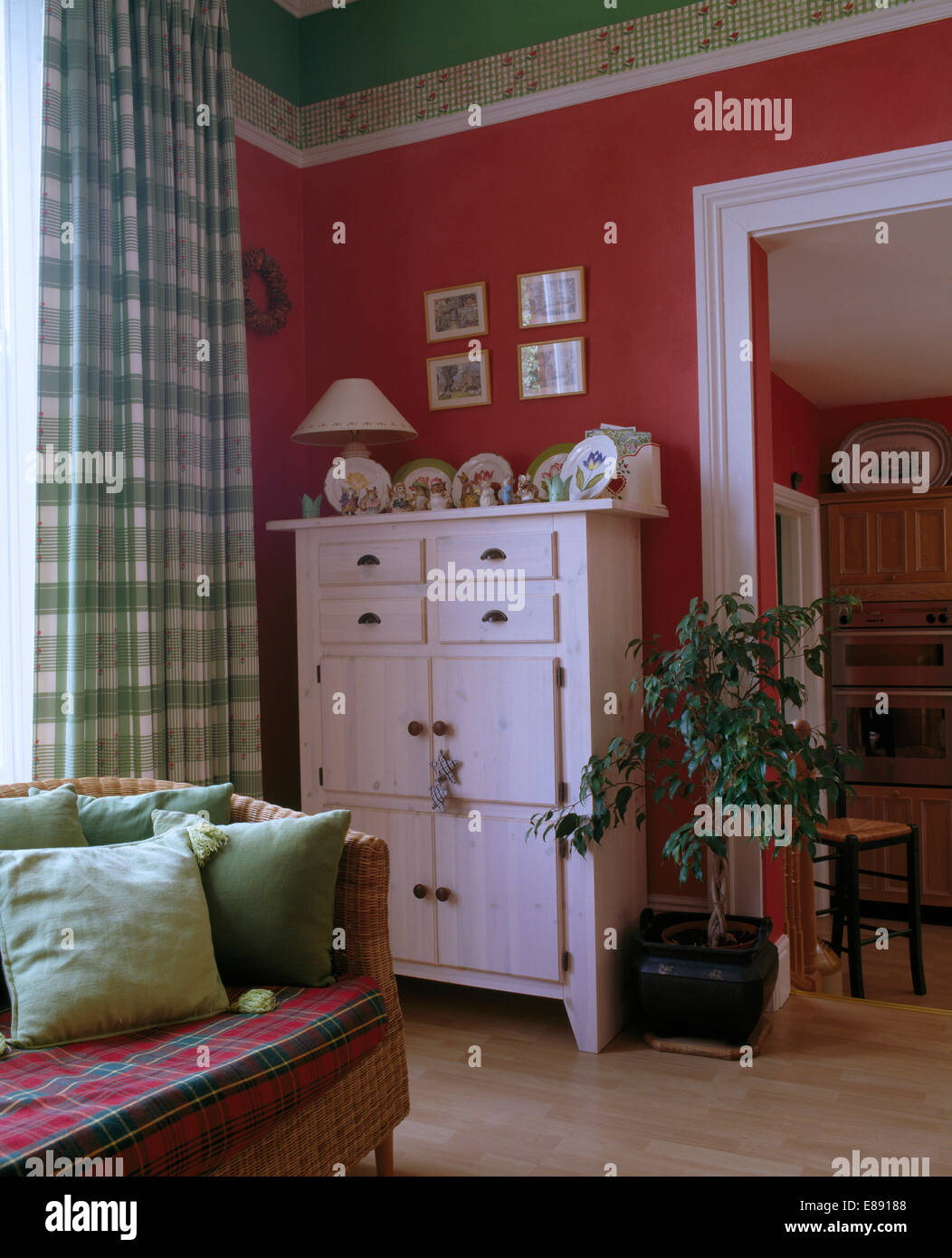 Weiß lackiertes Schrank in dunkelrosa Dining room mit grünen aufgegebenes Vorhängen und Sofa mit grünen Kissen Stockfoto