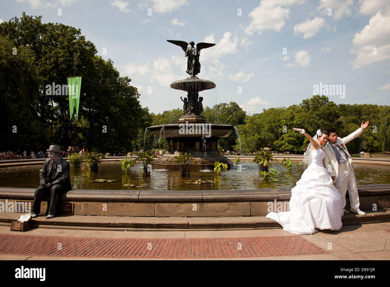 Eine verheiratetes Paar Pose für Hochzeitsfotos in Central Park, New York, mit einem Straßenkünstler saß in der Nähe. Bethesda-Brunnen im Hintergrund. Stockfoto