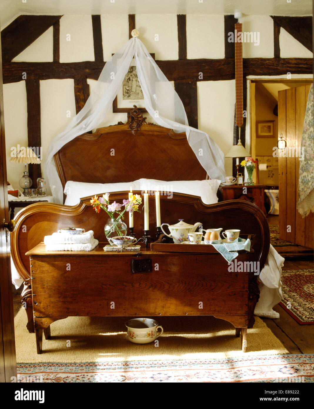 Frühstückstablett auf antiken Holzkiste am Fuße des antikes Bett mit weißen Voile Vorhänge in Land-Schlafzimmer Stockfoto