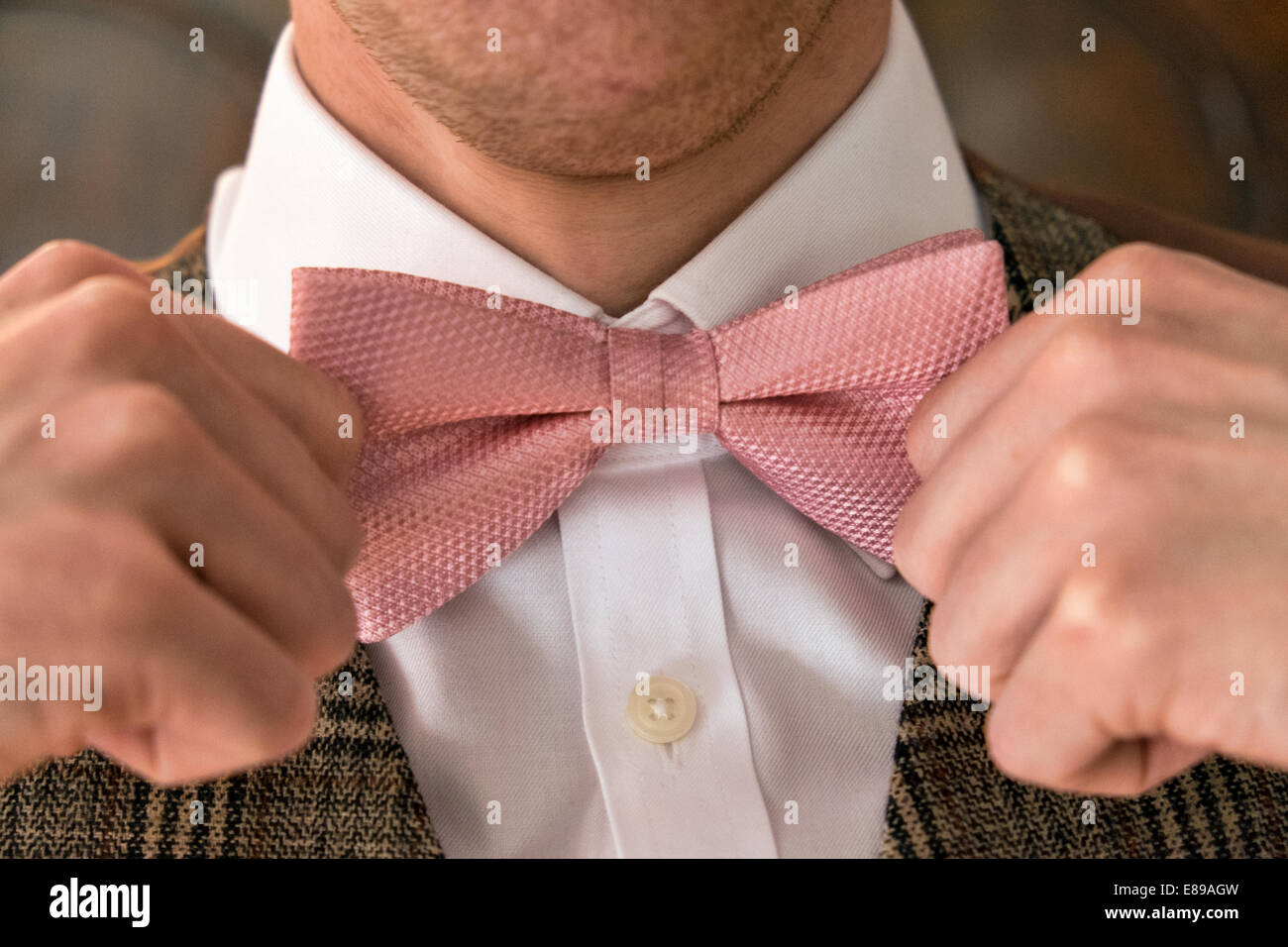 Ein gepflegten Gentleman einstellen Verschärfung seiner rosa Fliege und einen weißen Hemd & Tweed Anzug tragen Stockfoto