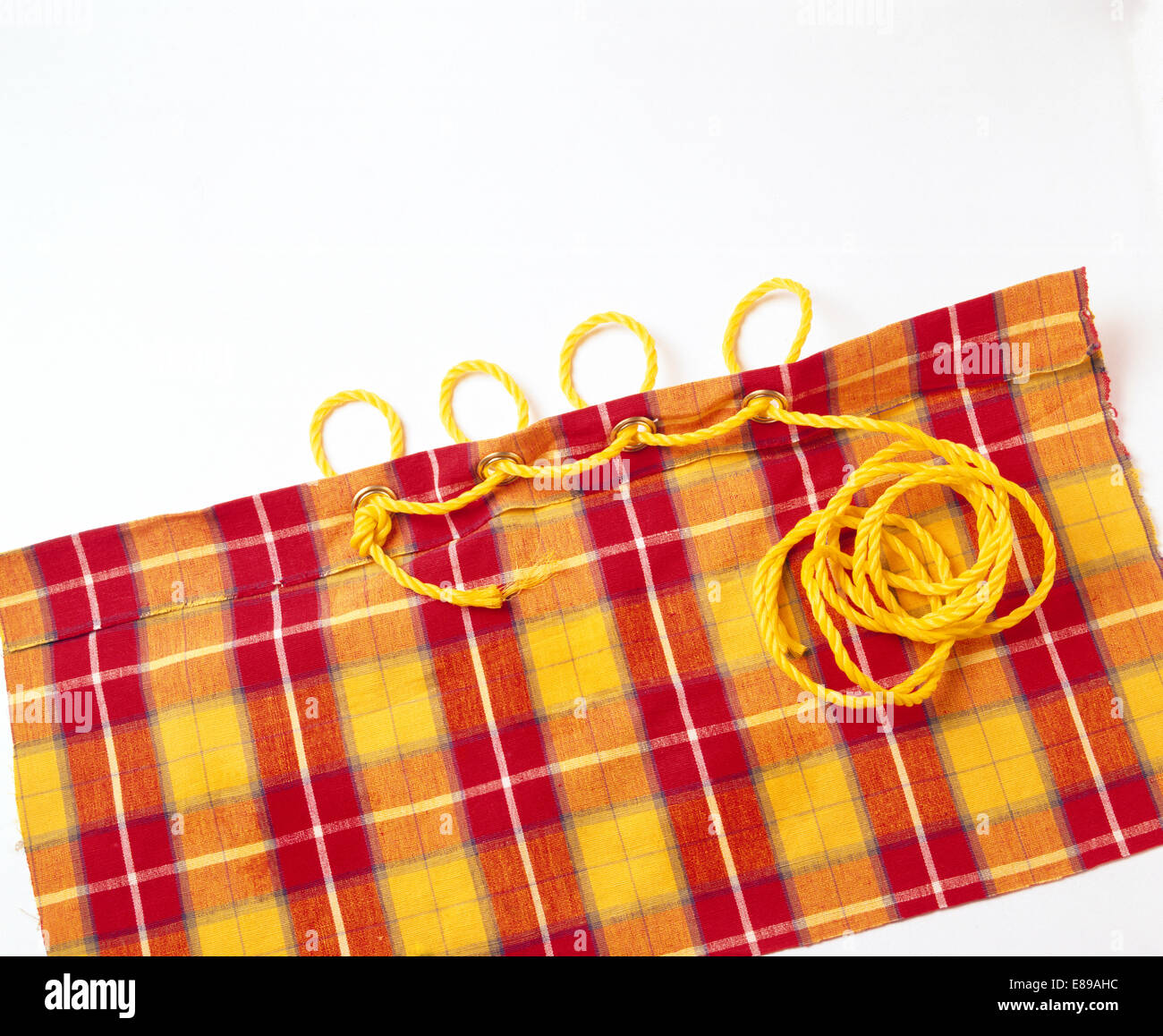 Nahaufnahme von rot + gelb karierten Vorhangstoff mit Ösen mit gelber Schnur gebunden Stockfoto