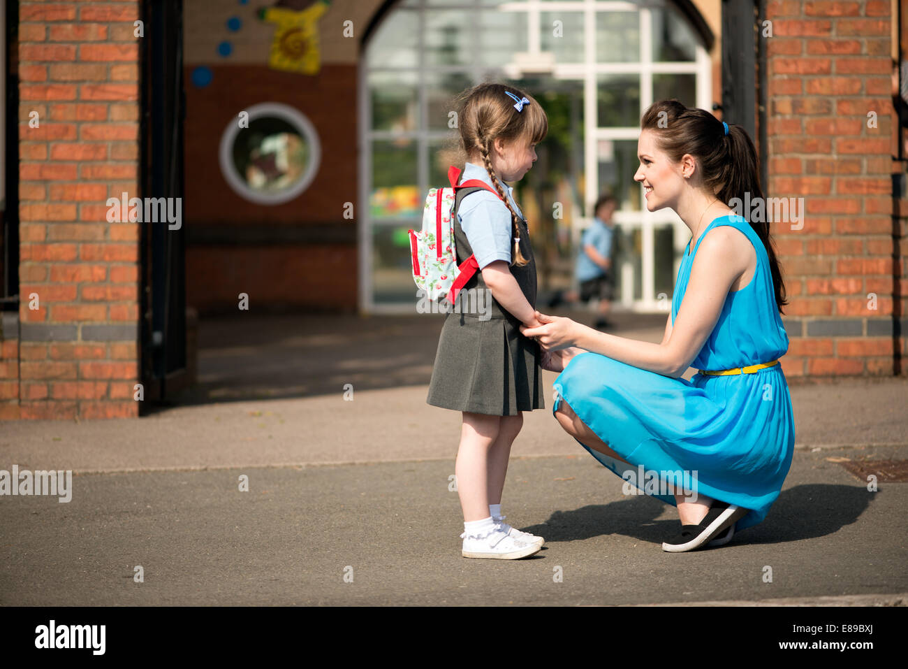 Eine attraktive, Lächeln, glücklich junge Mutter tröstet & aufnehmen oder ihre Tochter vor den Toren der Vorschule Abwurf Stockfoto
