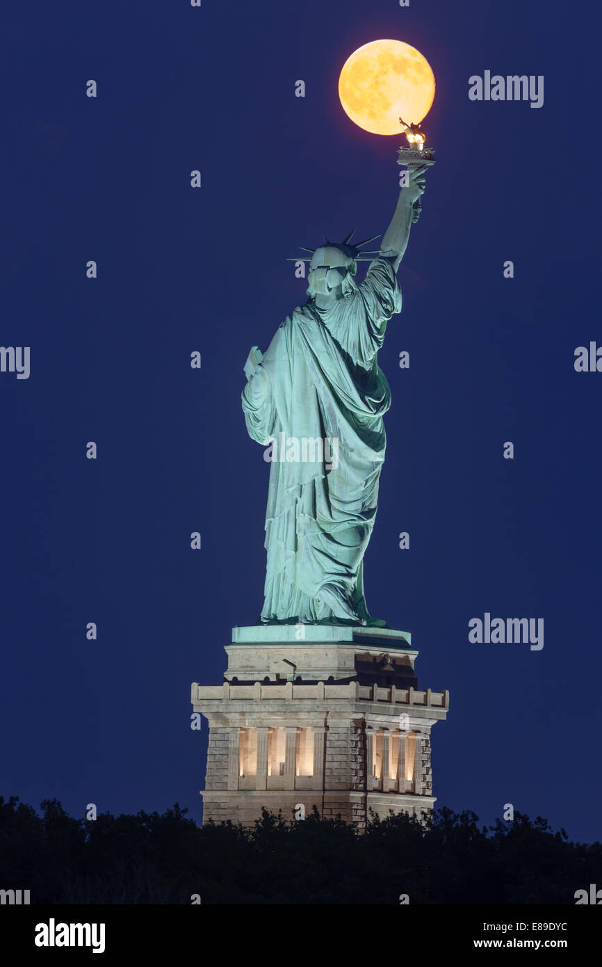 Der super Mondaufgang über die New Yorker Freiheitsstatue während der blauen Stunde. Stockfoto