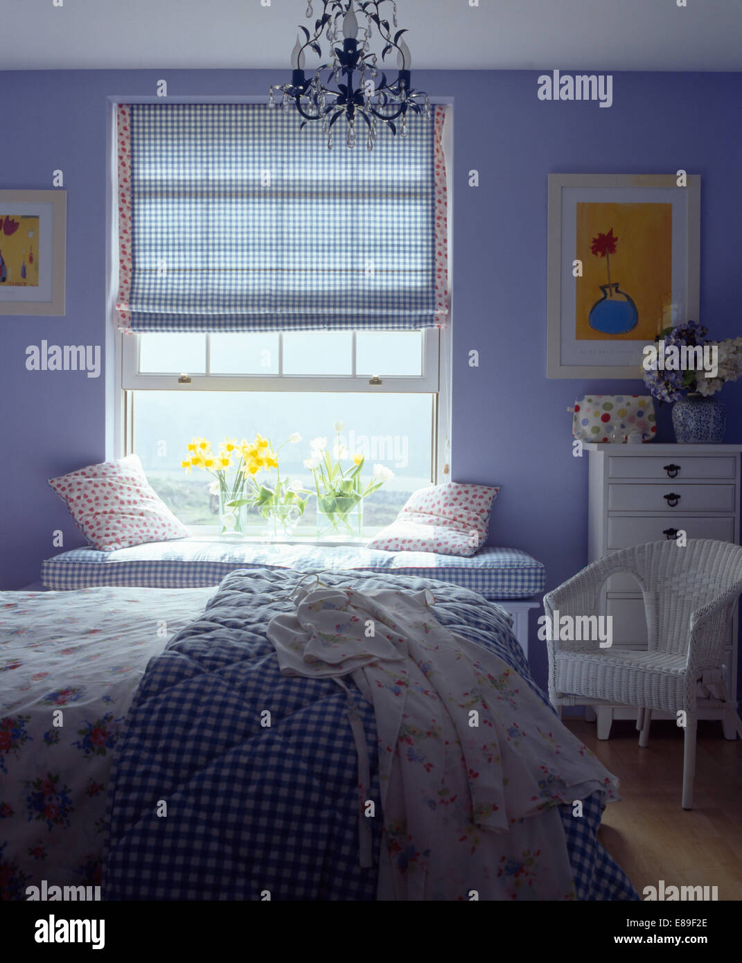 Blaue aufgegebenes Blind auf Fenster in lila Schlafzimmer mit weißen Lloyd Loom Stuhl und Bett mit aufgegebenen quilt Stockfoto