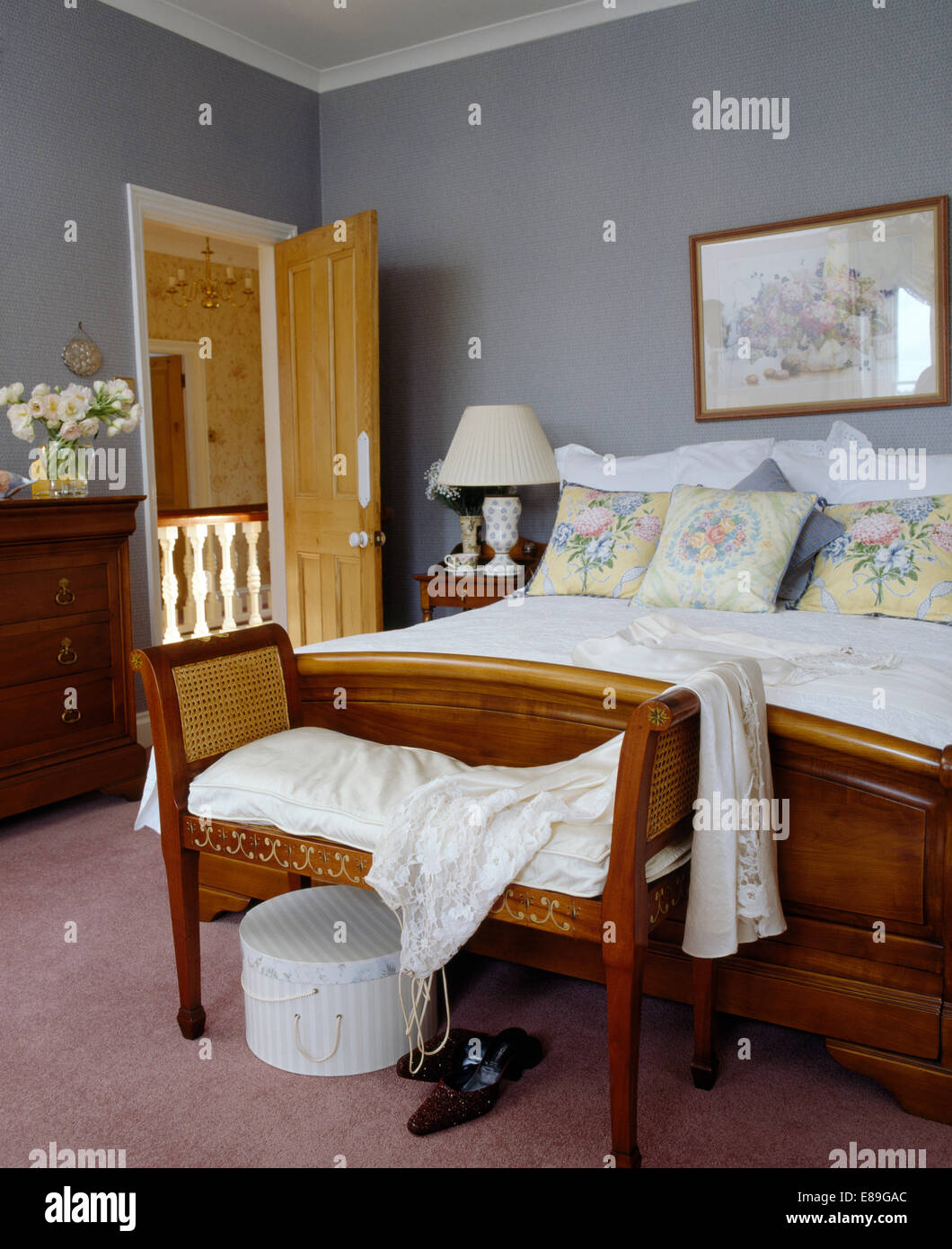 Rohrstock zurück Hocker am Fuße des Holzbett mit floralen Kissen in grau Schlafzimmer Stockfoto
