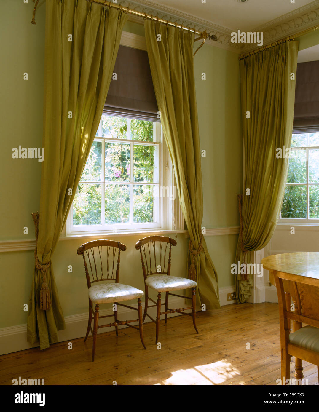 Bettwäsche Vorhänge und grüne Vorhänge am Fenster über einfache Stühle in blass grün Schlafzimmer mit Holzboden Stockfoto