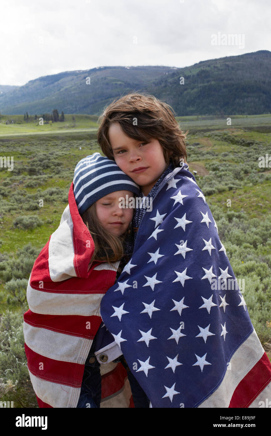Bruder und Schwester gewickelt in amerikanische Flagge im Feld Stockfoto