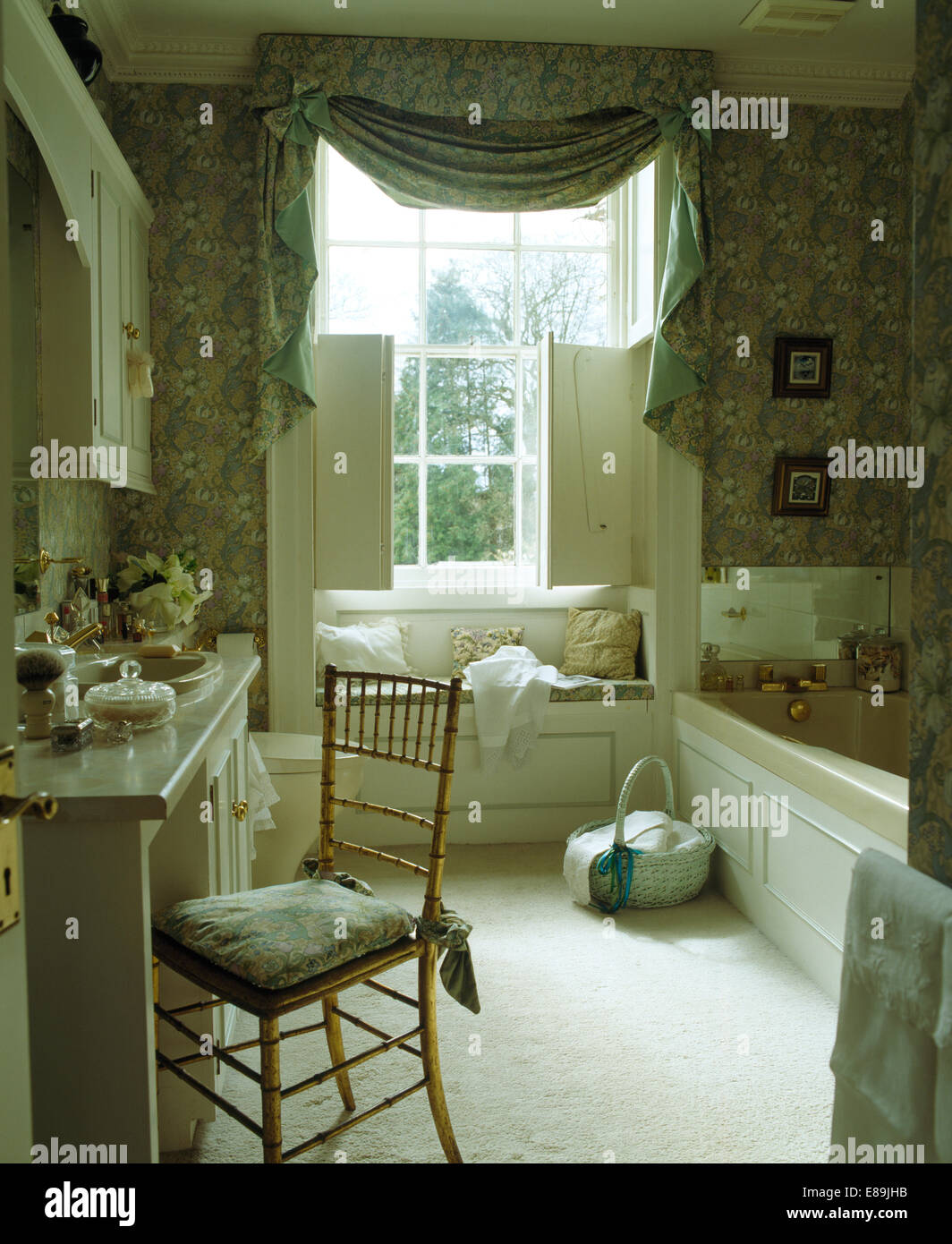 Swagged + tailed Profilkranz auf Fenster mit weißen Fensterläden im Badezimmer mit weißen Teppich und Mustertapeten Stockfoto