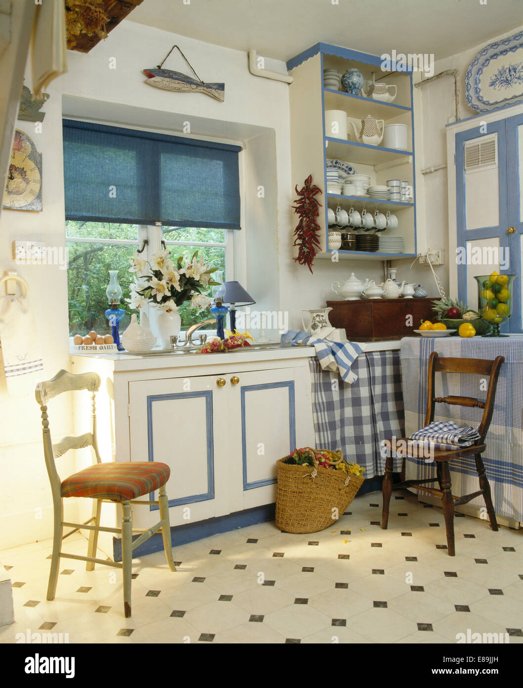 Blaue Blind auf Fenster über dem Waschbecken in blau + weiß ausgestattete Einheit in weiße Landhausküche mit Vinyl-Fliesenboden Stockfoto
