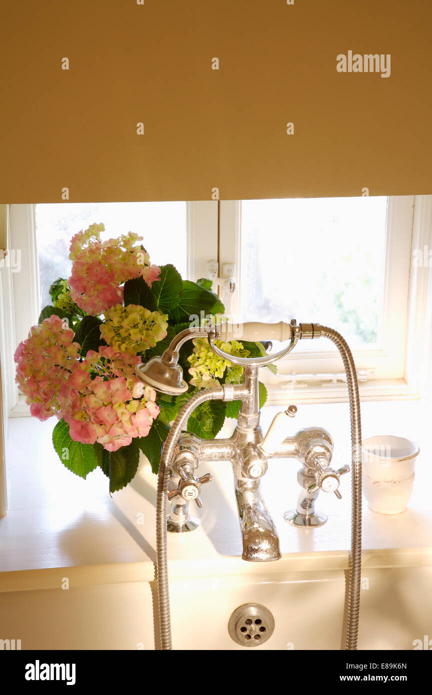 Beige blind über Chrom-Duschkopf und Wasserhähne und Vase mit rosa Hortensien Stockfoto