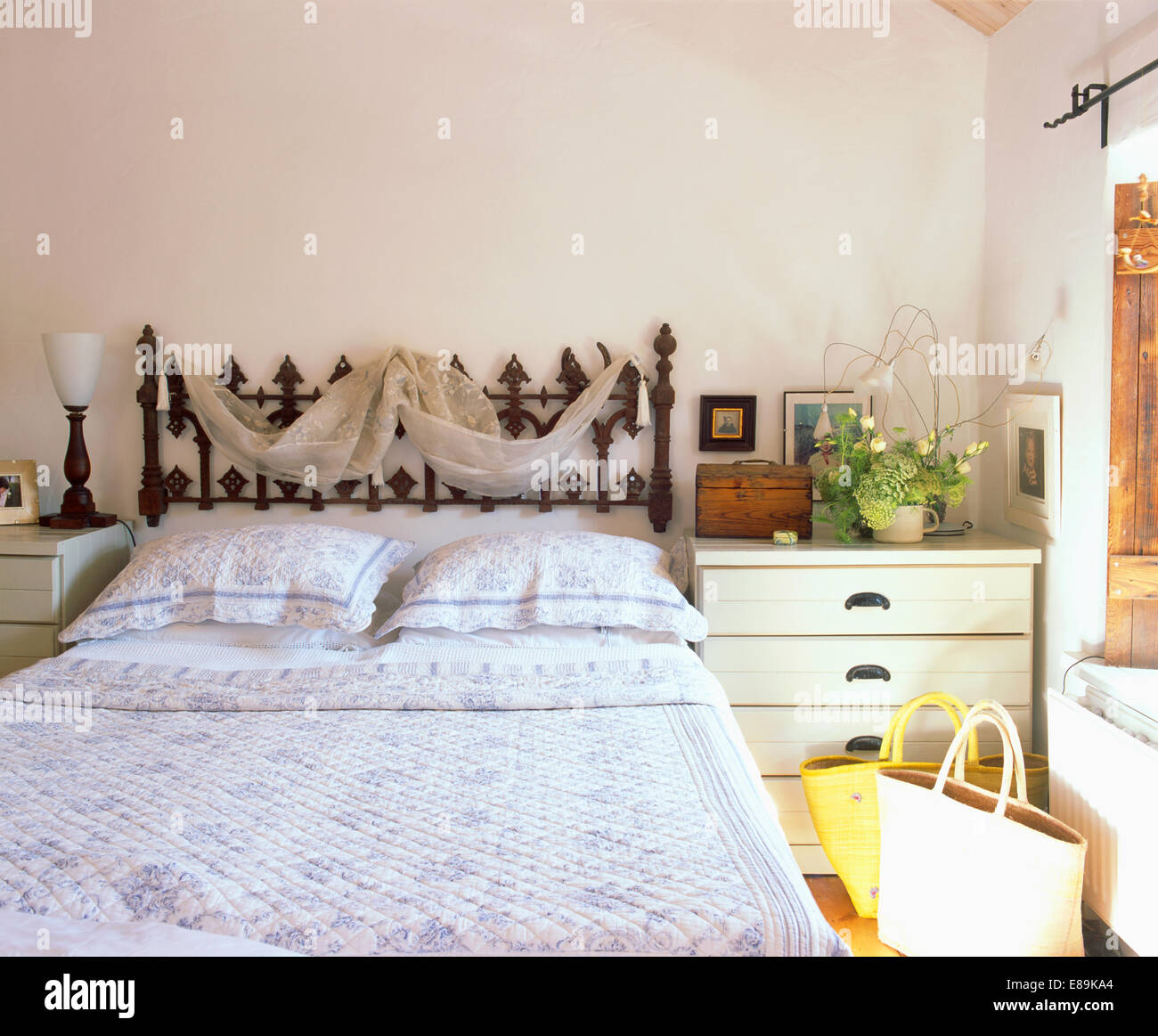 Voile drapieren auf reich verzierten schmiedeeisernen Bett mit blau + weiß floral Steppdecke und Kissen in kleine weiße Schlafzimmer Stockfoto